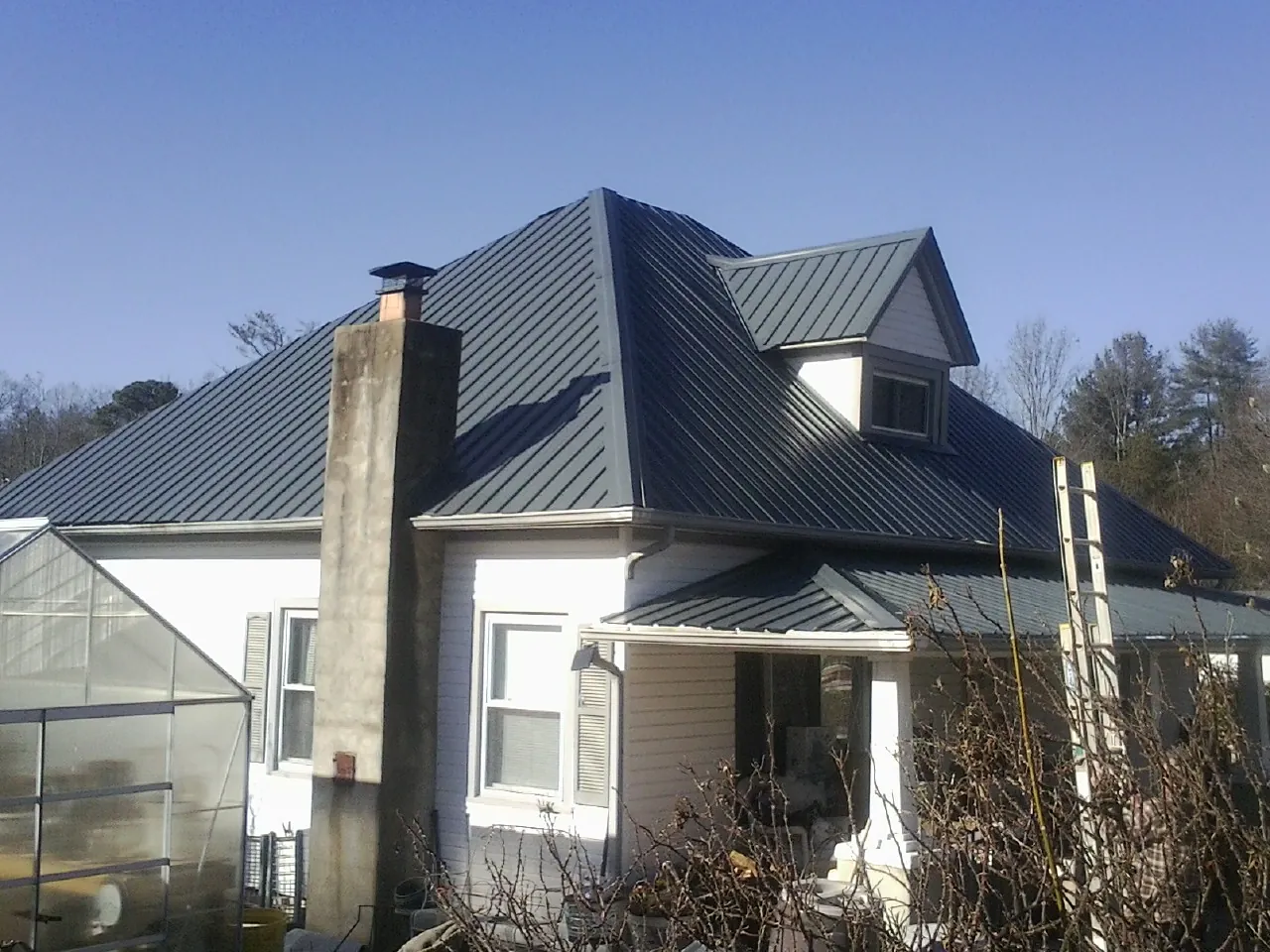 Dark blue standing seam metal roof on a white farmhouse with dormer — Slate & Tile Roof Repair by Roofing Brothers in Rock Island