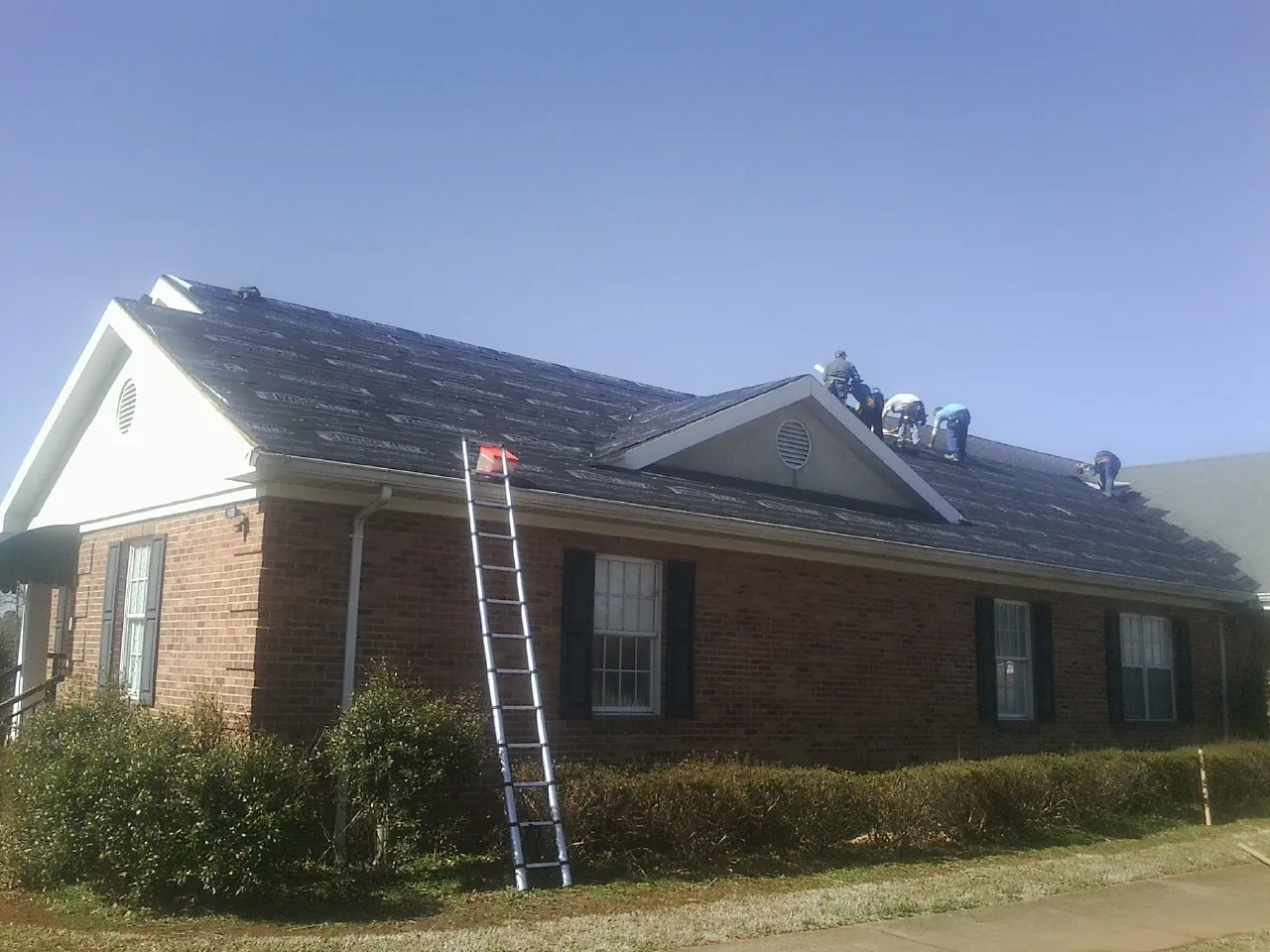 Crew tearing shingles off a brick ranch roof with a ladder set — Metal Roof Repair work by our crew in Rock Island