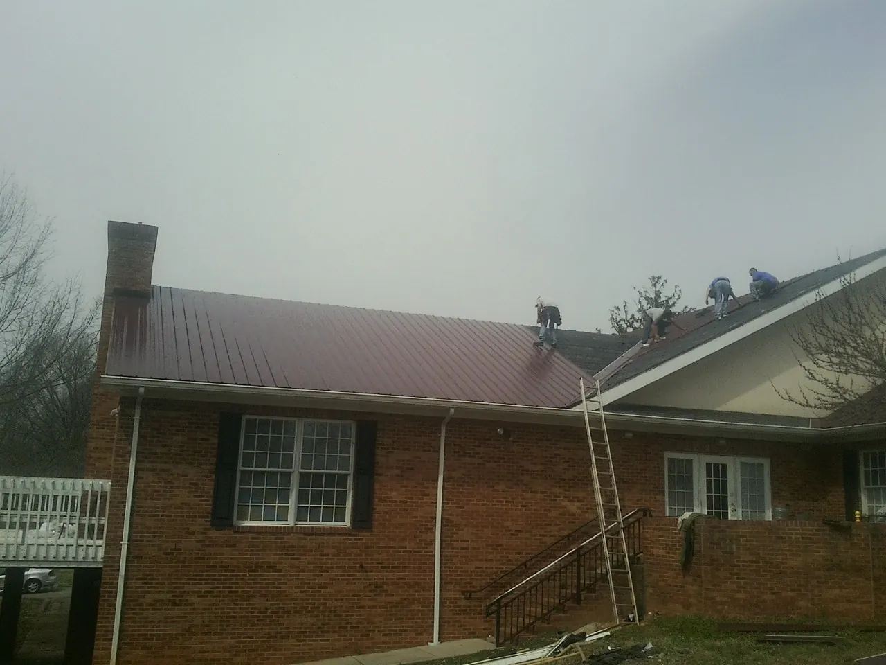 Crew setting red metal roofing panels on a brick home in Rock Island